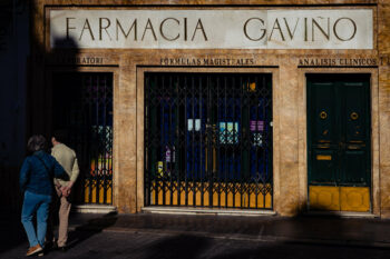 Un homme et une femme passent devant une pharmacie avec une pancarte indiquant farmacia gavino en Andalousie.