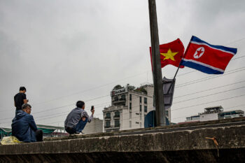 Un groupe de personnes assises sur un rebord avec des drapeaux vietnamiens flottants.