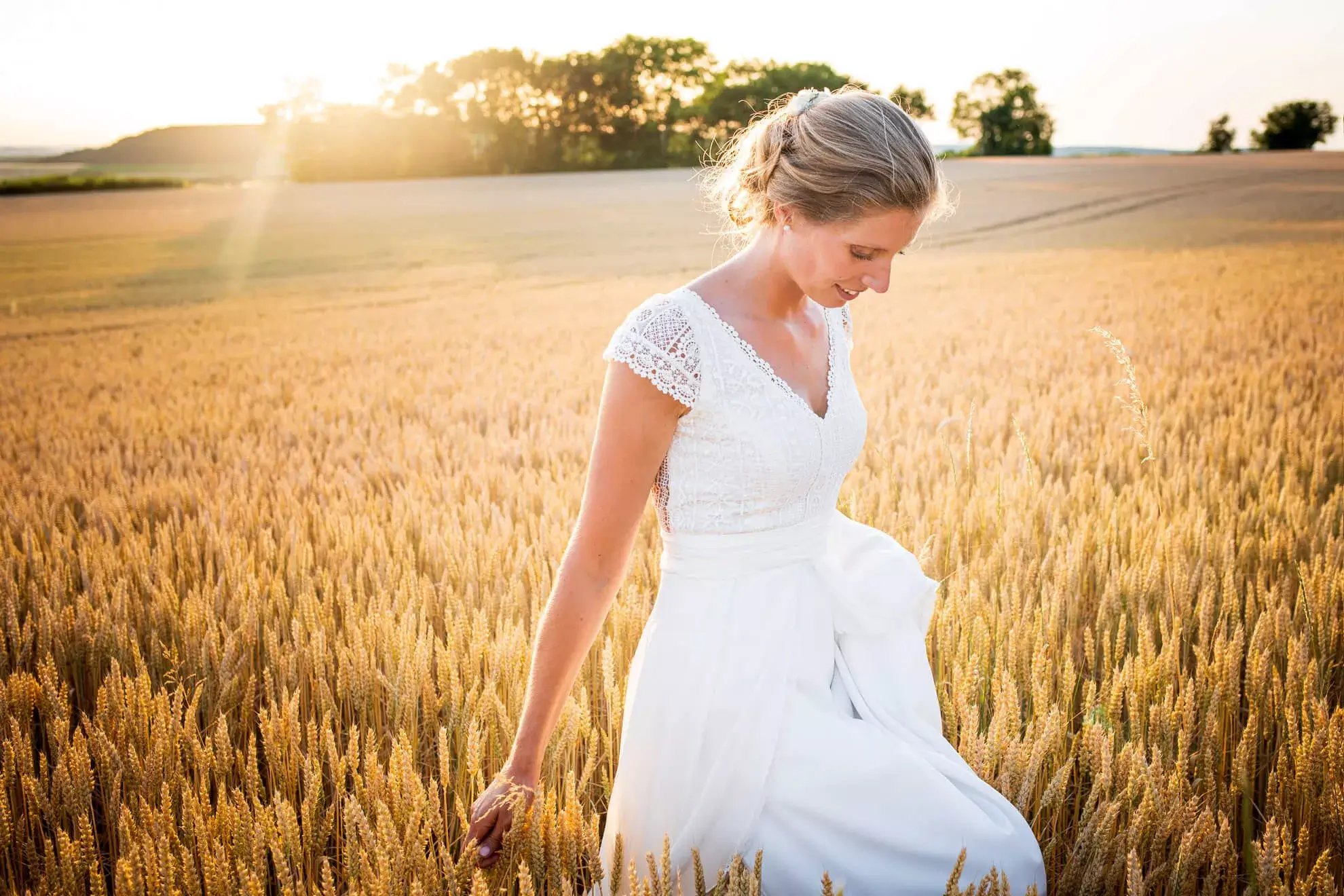 Une jeune mariée au milieu d'un champ au couché du soleil.