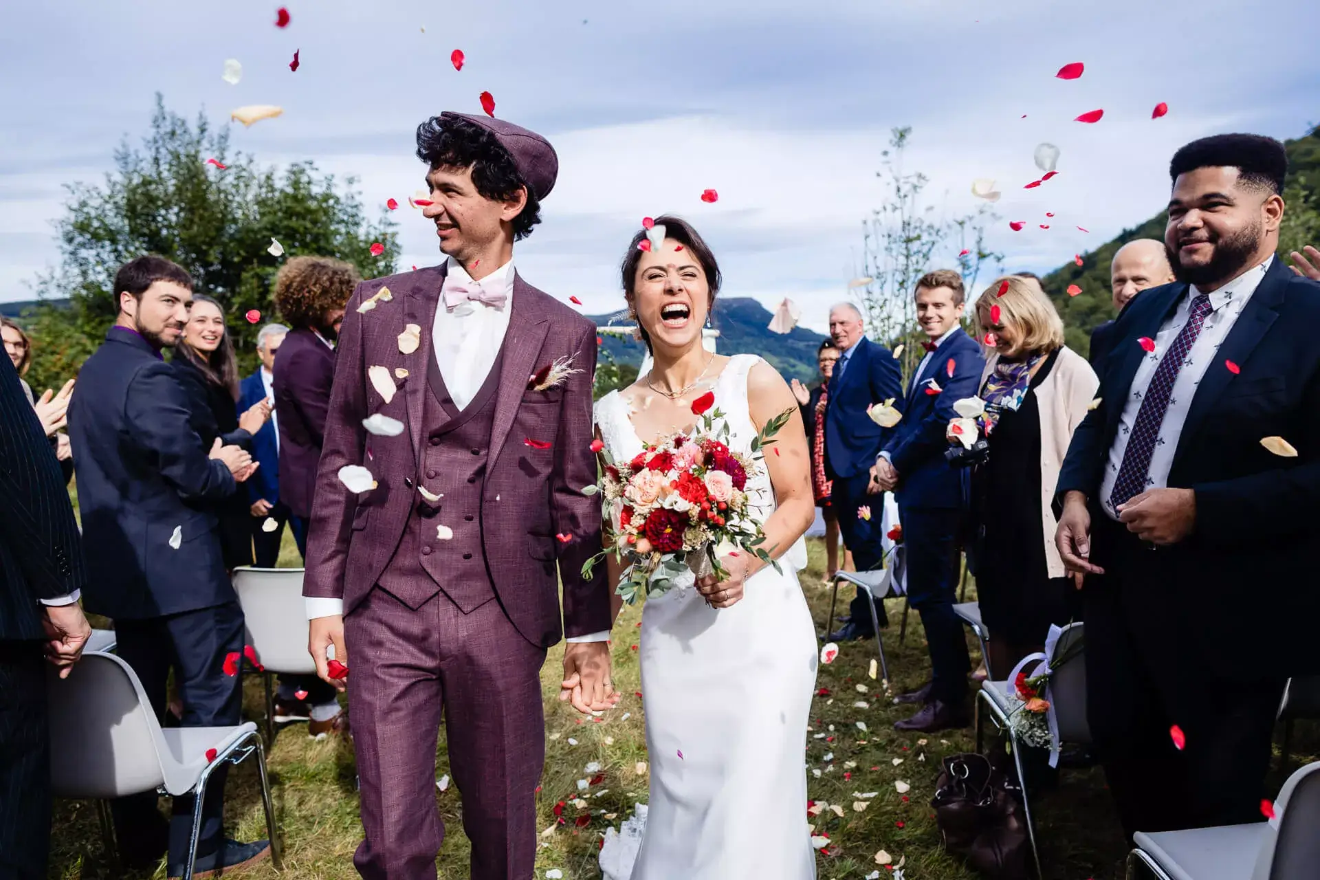 La marié avec son bouquet de fleurs, aux coté de son mari, au milieu des pétales lancés par les invités.