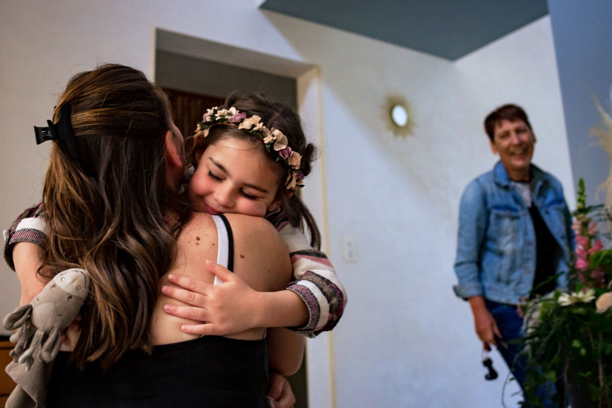 Une femme serre dans ses bras une petite fille dans une maison, peut-être pendant les préparatifs du mariage.