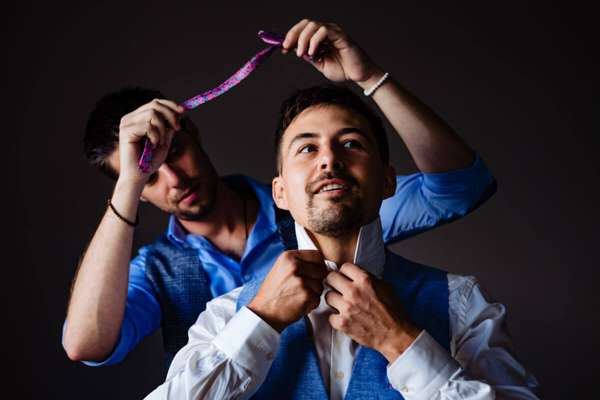 Deux hommes préparant une cravate pour un mariage sur fond sombre.