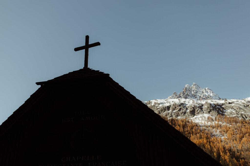 A church with a cross in front of a majestic mountain.