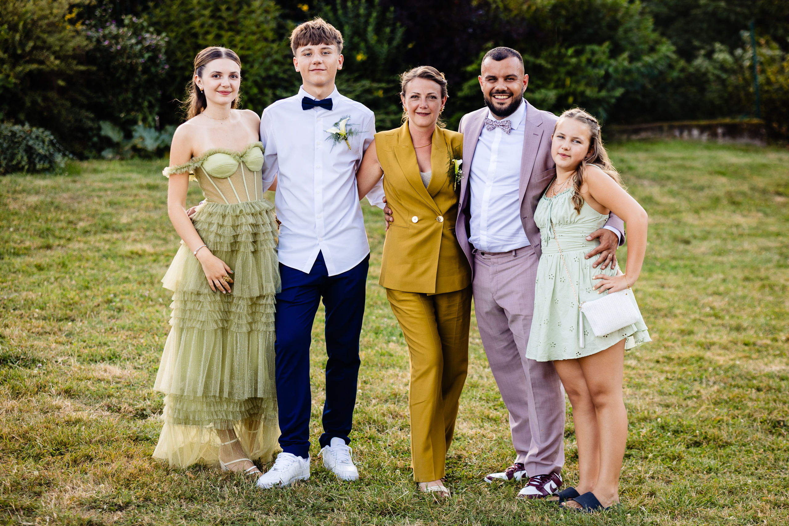 Groupe de cinq invités en tenues formelles sur l'herbe de la Ferme Sainte-Anne, mariage Langres