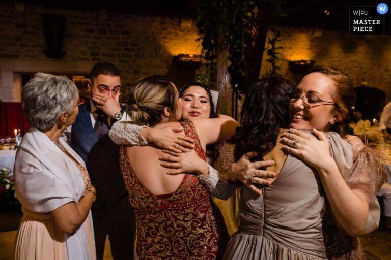 Étreinte collective entre invitées pendant la soirée, le marié ému en arrière-plan.